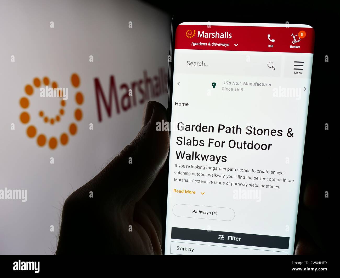 Person holding cellphone with webpage of British landscaping products company Marshalls plc in front of logo. Focus on center of phone display. Stock Photo