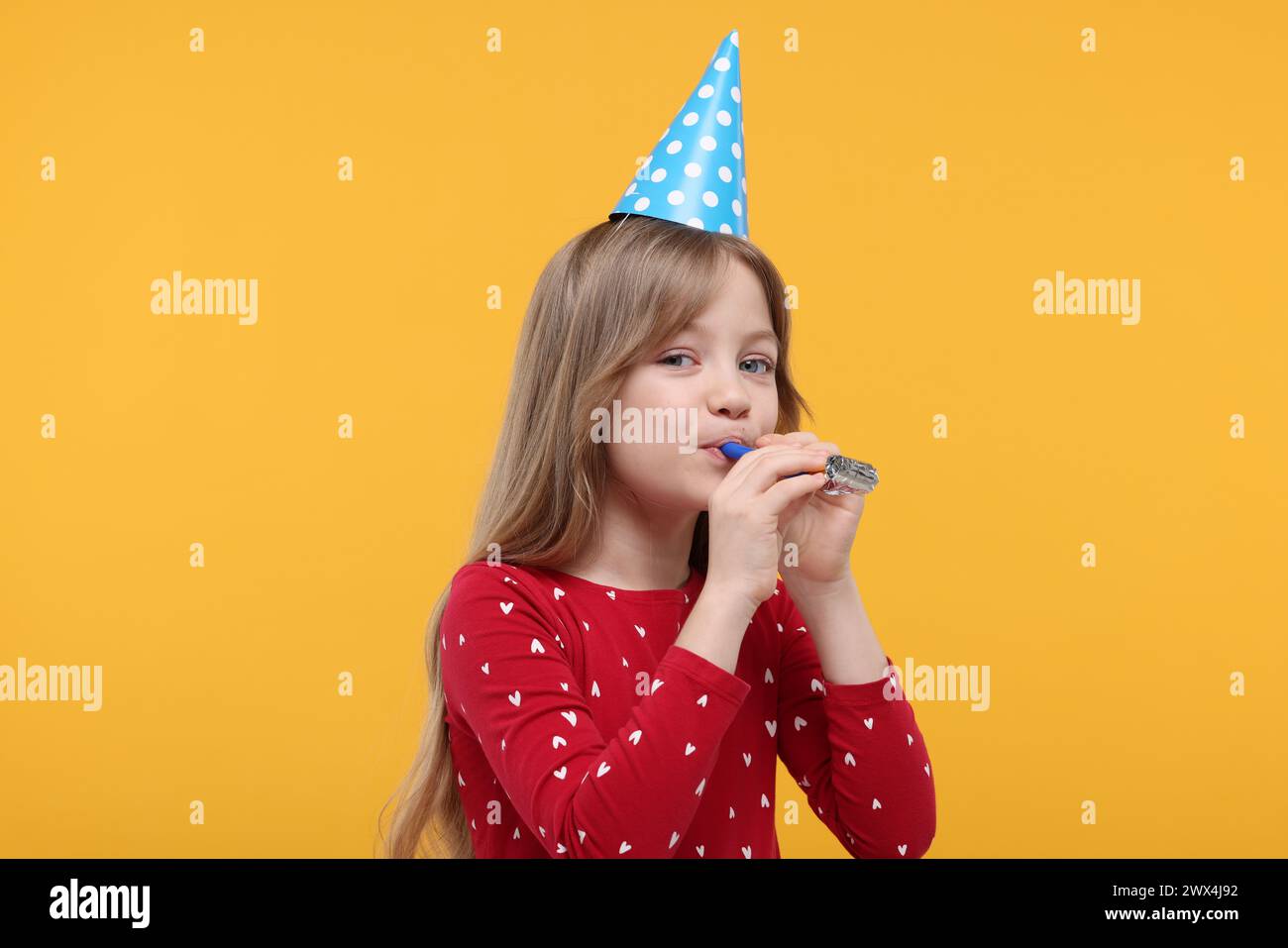 Cute little girl in party hat with blower on yellow background Stock ...