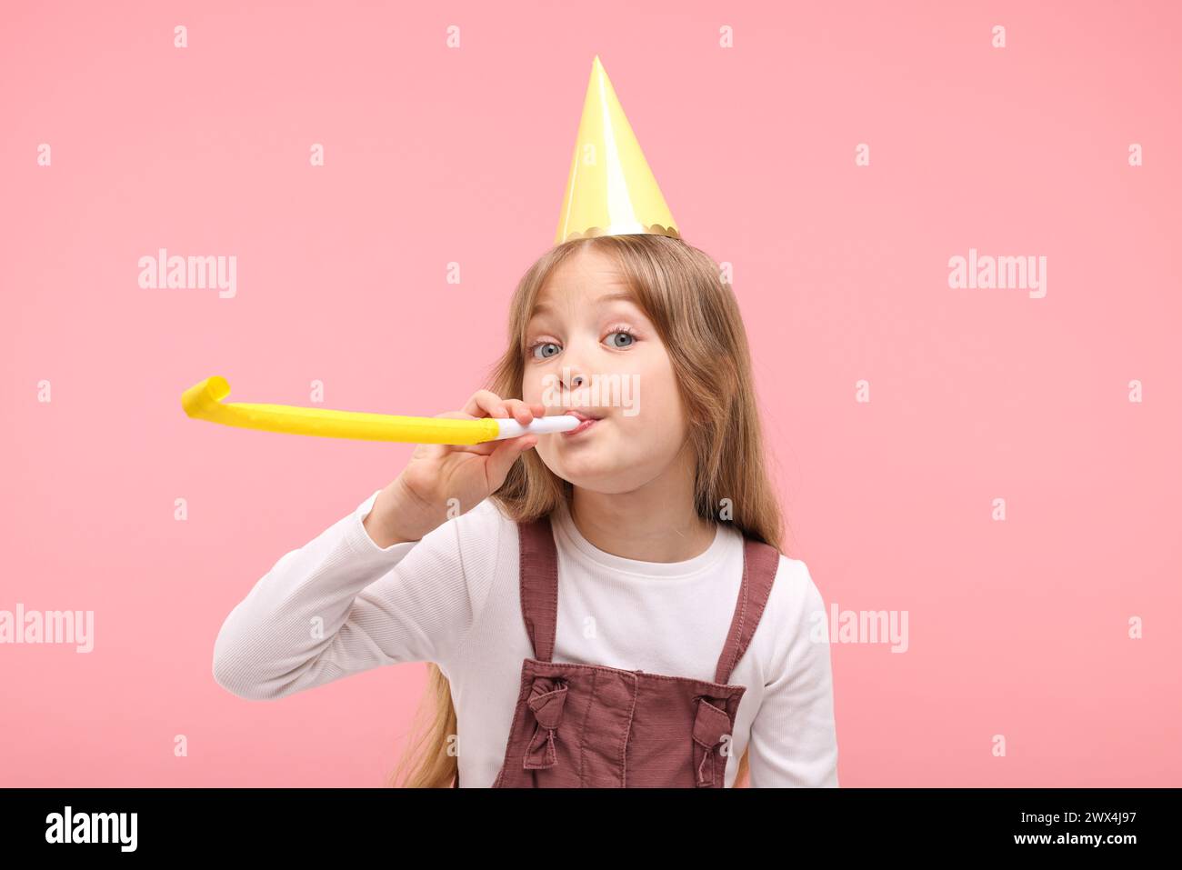 Cute little girl in party hat with blower on pink background Stock ...