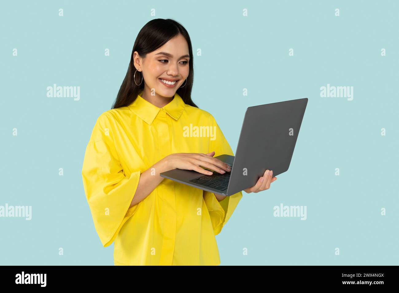 Young happy hispanic lady using laptop, typing report marketer, isolated at blue color background.  Stock Photo