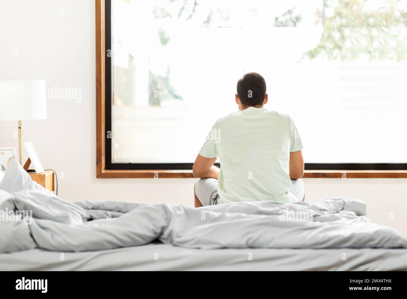Man sitting on bed facing window Stock Photo Alamy