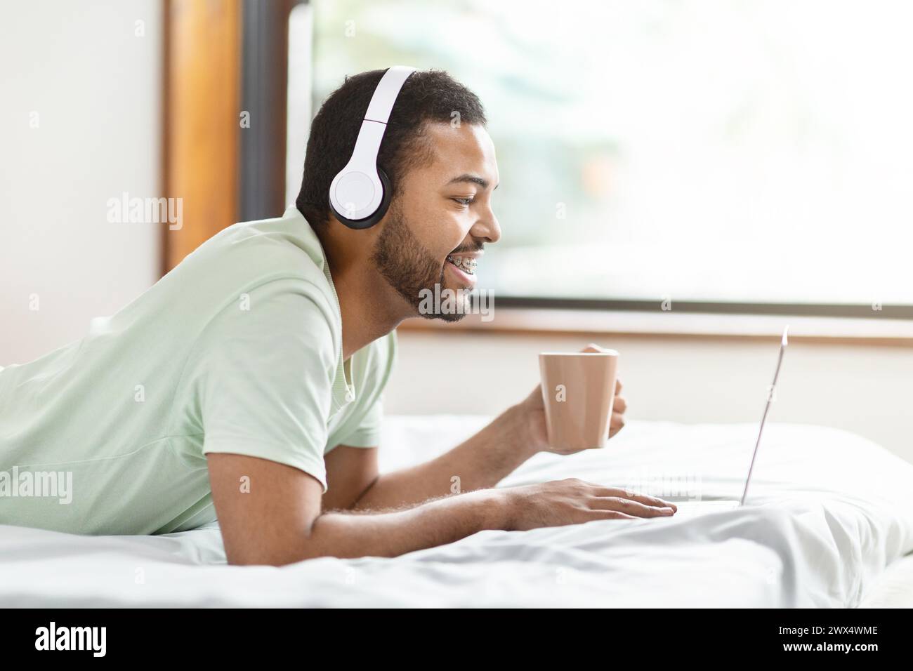 Man in bed with headphones using laptop Stock Photo