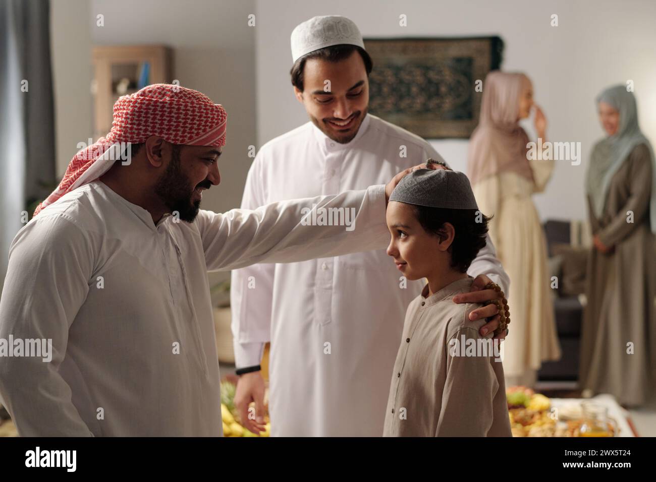 Cheerful bearded Middle Eastern man patting his nephew on head at family gathering on Uraza Bayram day Stock Photo