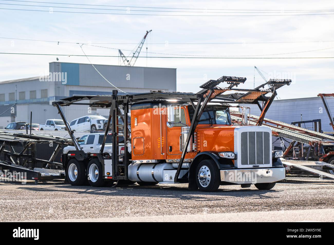 Industrial carrier orange car hauler big rig semi truck tractor with empty two level hydraulic semi trailer standing on the warehouse parking lot wain Stock Photo