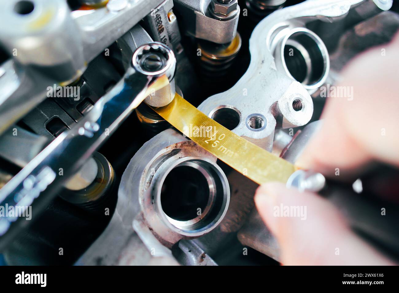 Car mechanic checking and adjusting valves of car engine with feeler