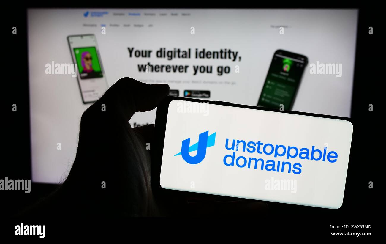 Person holding mobile phone with logo of American blockchain company Unstoppable Domains Inc. in front of web page. Focus on phone display. Stock Photo