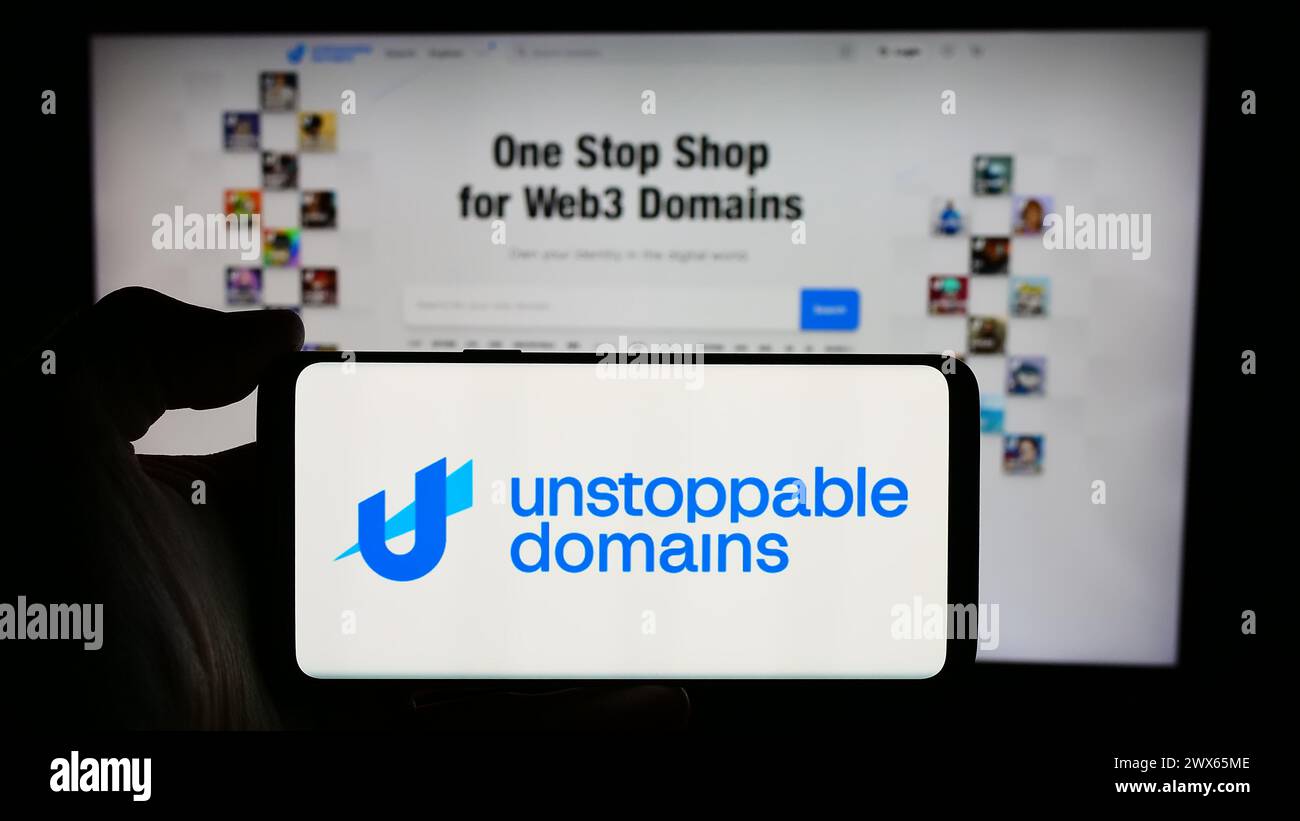 Person holding cellphone with logo of US blockchain company Unstoppable Domains Inc. in front of business webpage. Focus on phone display. Stock Photo