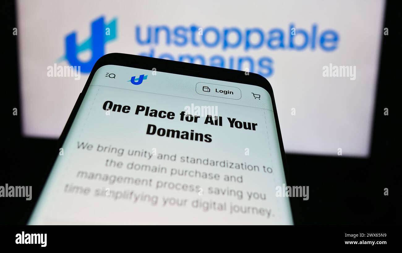 Smartphone with website of US blockchain company Unstoppable Domains Inc. in front of business logo. Focus on top-left of phone display. Stock Photo