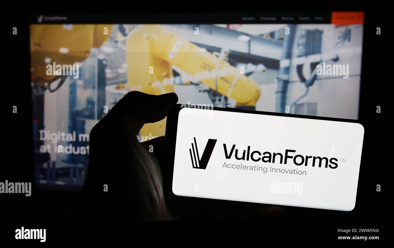 Person holding mobile phone with logo of American digital manufacturing company VulcanForms Inc. in front of web page. Focus on phone display. Stock Photo