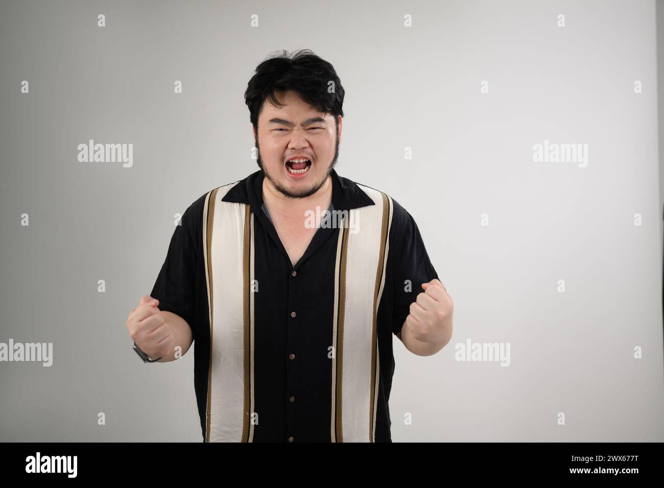 Horizontal shot of angry man shouting with clenched fists on white background Stock Photo