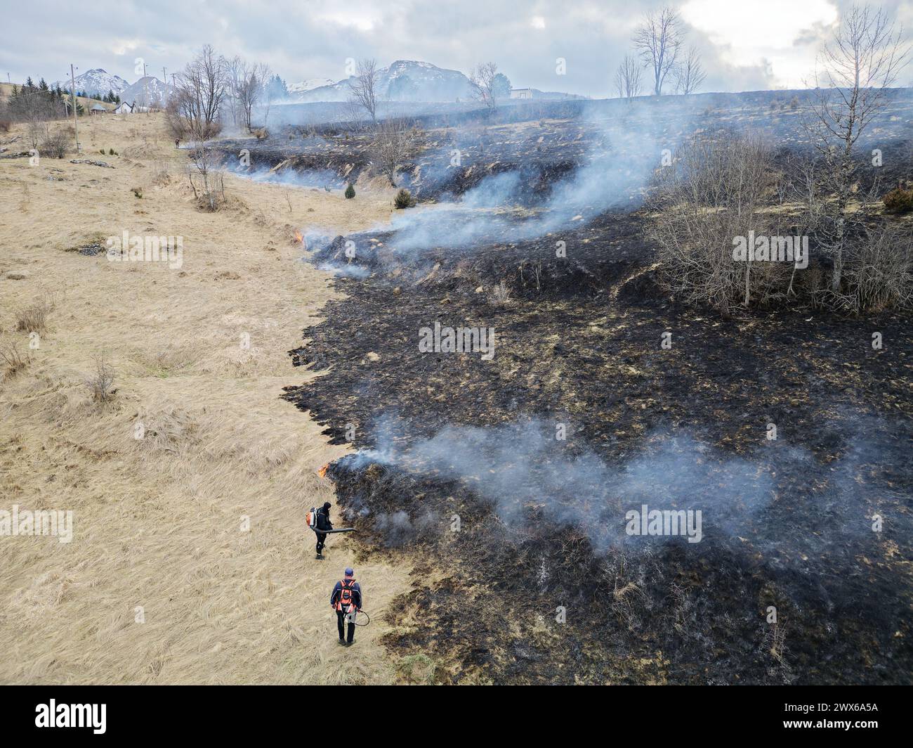 Two firemen extinguish a fire. Burning field. Wildfire in the mountains. Forest fire. Stock Photo