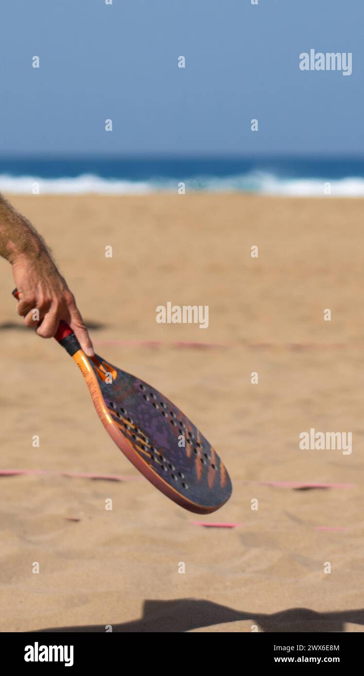 Man's hands with tennis racket on the beach with a background of sand and sea Stock Photo