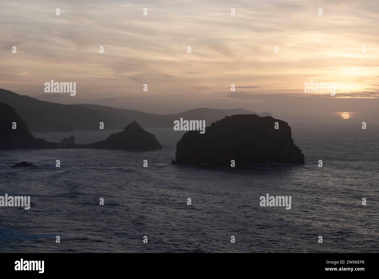 serene sunset over the ocean, highlighting silhouetted islands and illuminating the sky with soft, warm hue Stock Photo