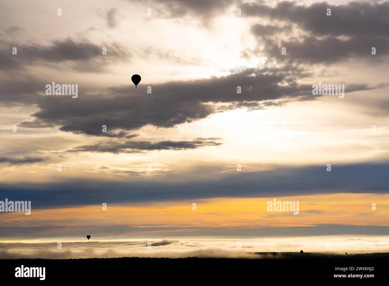 Hot air balloon flying at dawn over a blanket of clouds Stock Photo