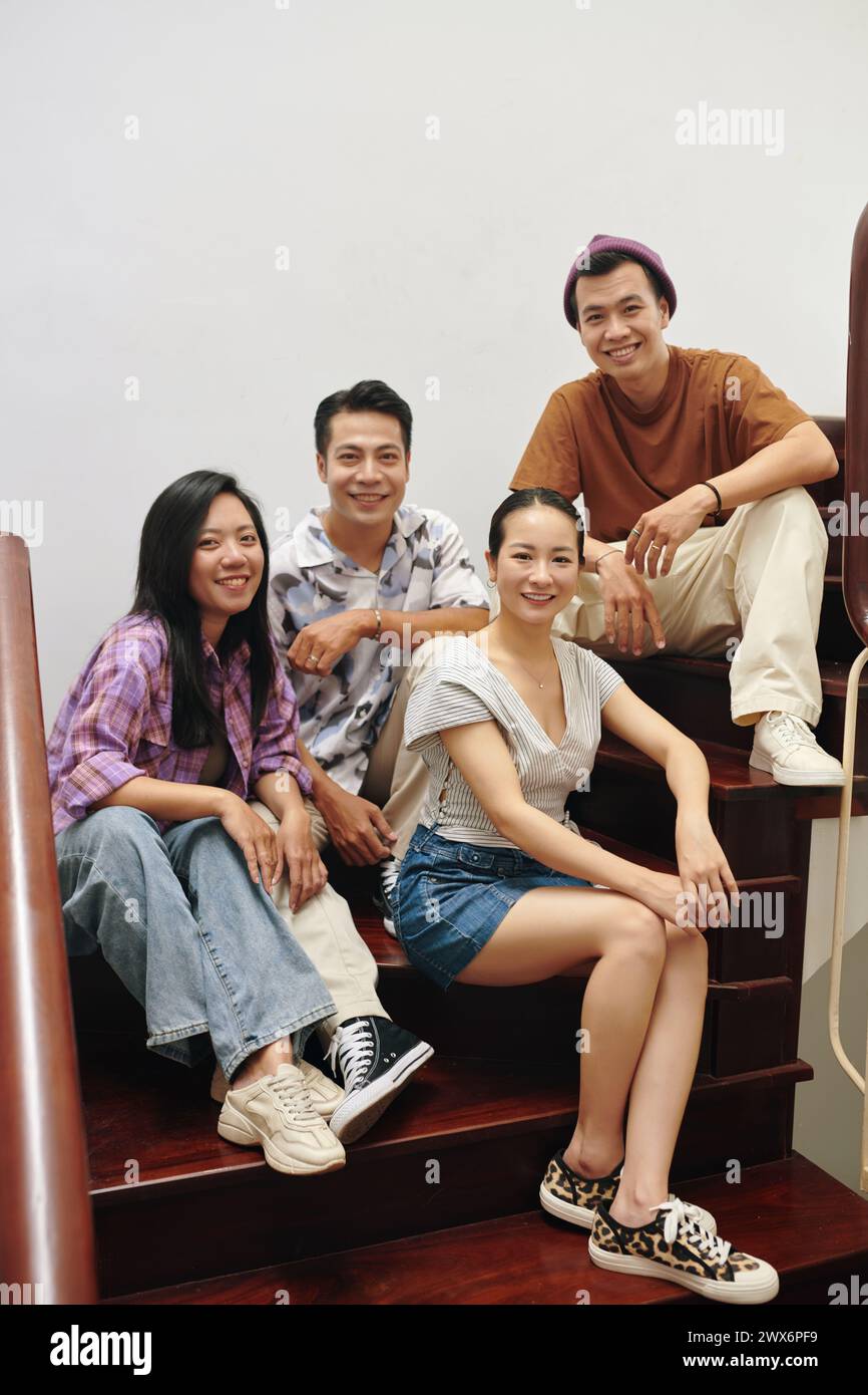 Smiling Vietnamese young people sitting on wooden steps at home Stock Photo