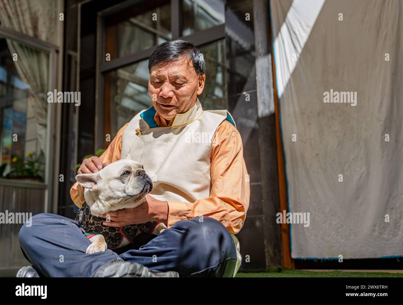 (240328) -- LHASA, March 28, 2024 (Xinhua) -- Phutsering plays with a dog at home in Lhasa, southwest China's Xizang Autonomous Region, March 23, 2024. Born in 1944 in Bainang County of Xigaze City, Phutsering was raised in a former serf family. A humble shack, situated near the manor where his mother toiled as a serf, served as his childhood home. Meanwhile, his father, employed at a separate manor, struggled to make ends meet by farming and crafting during lean months, barely generating sufficient income to cover the rent and taxes for their dwelling and fields. At the age of thirteen, he gr Stock Photo