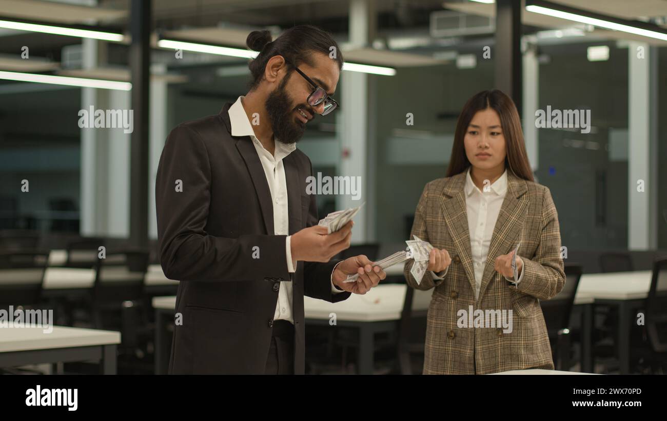 Inequality equal pay racial gender discrimination patriarchal world Indian business man Asian woman in office counting money finance salary cash Stock Photo