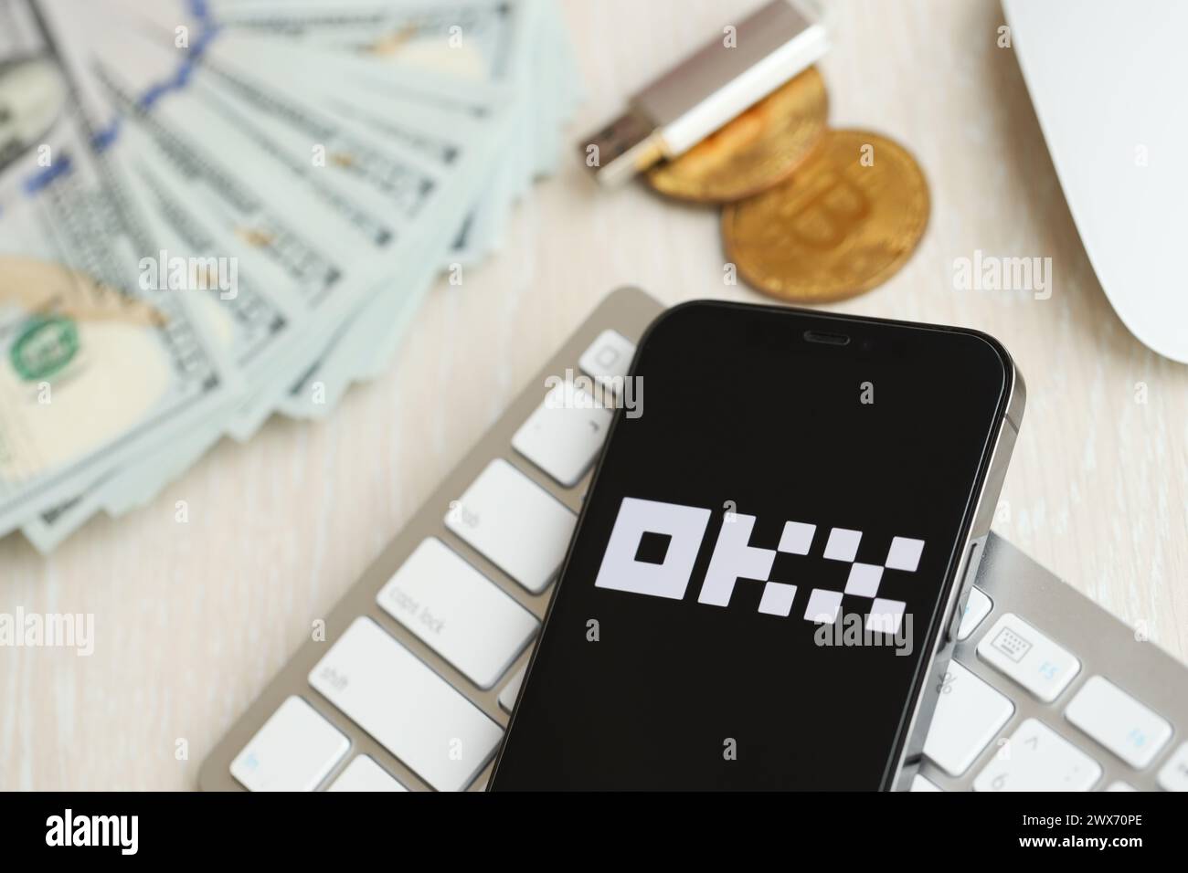 KYIV, UKRAINE - MARCH 15, 2024 OKX logo on iPhone display screen on white keyboard with money and bitcoins. Cryptocurrency exchange portal Stock Photo