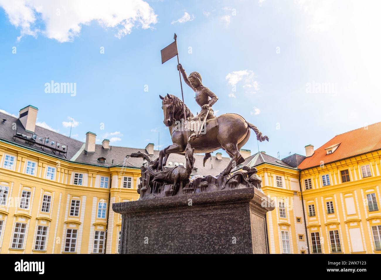 The bronze statue of Saint George triumphantly slays a dragon, set against the vibrant backdrop of Prague Castle under a blue sky. Prague, Czechia Stock Photo