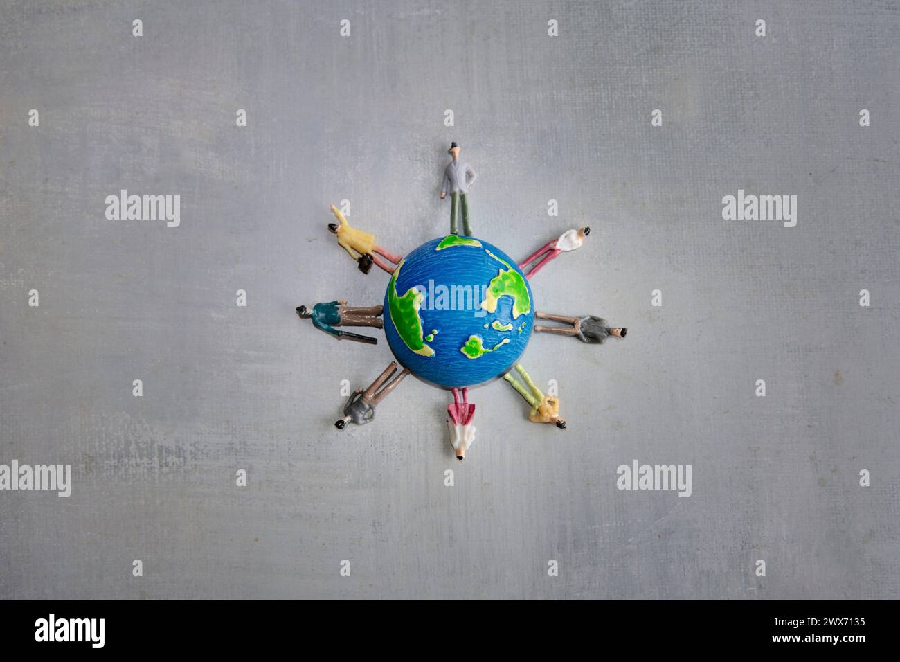 A group of miniature toy people in various colors stand around a globe on a gray surface. Copy space for text. Earth day, diversity and multiracial Stock Photo