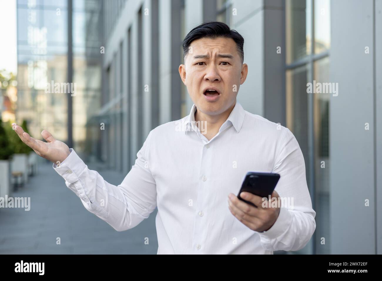 Closeup portrait of an angry young Asian man in a white shirt standing