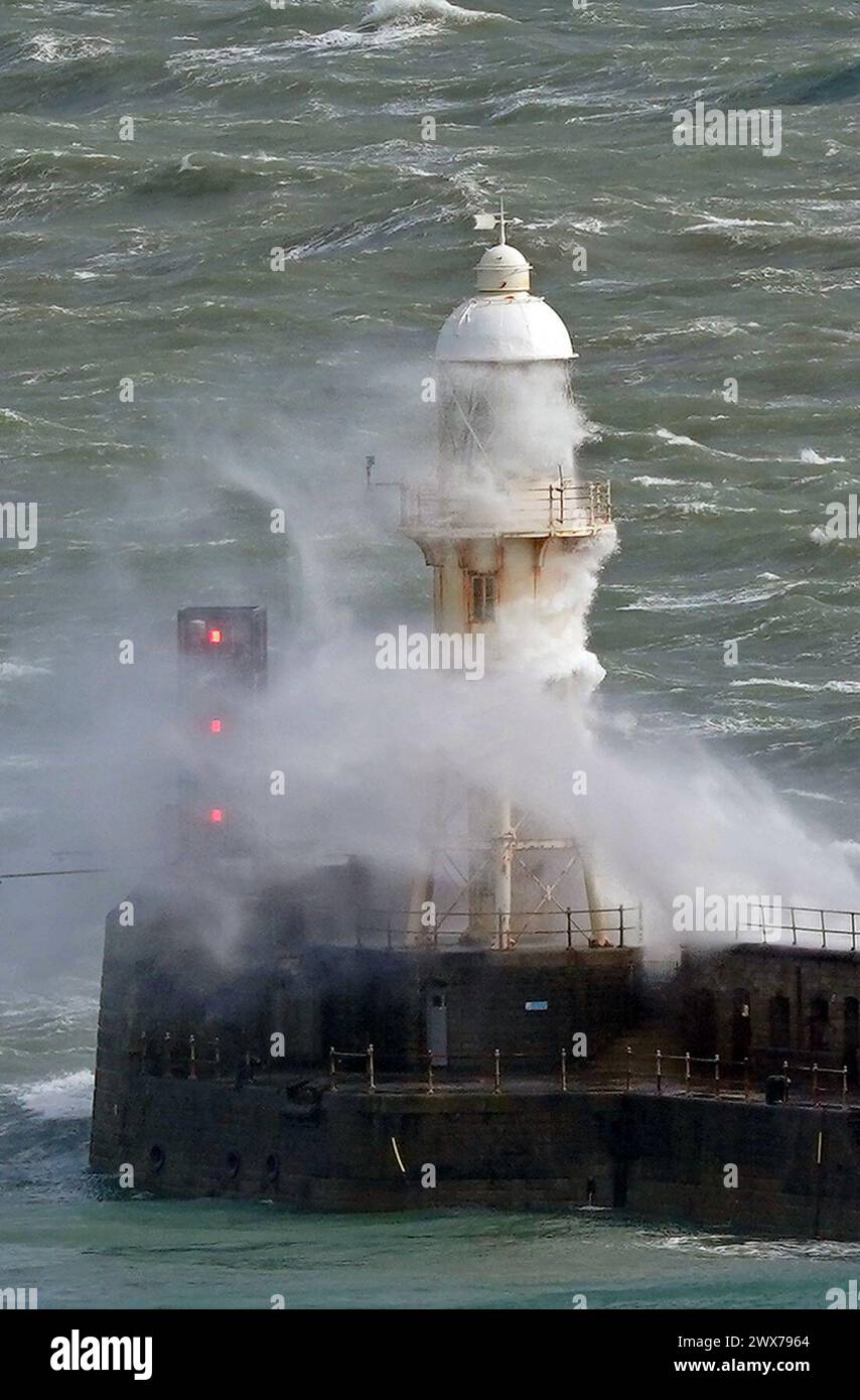 Waves crash over a lighthouse on the harbour wall in Dover, Kent. Forecasters say an area of rain, sleet and hill snow is moving north across the UK as holidaymakers prepare to embark on Easter getaways. Picture date: Thursday March 28, 2024. Stock Photo