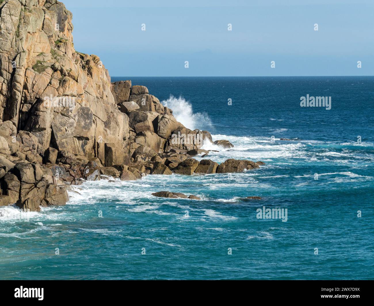 Waves breaking on rocky Cornish granite headland near Porthcurno on a sunny day with clear blue sky, Cornwall, England, UK Stock Photo