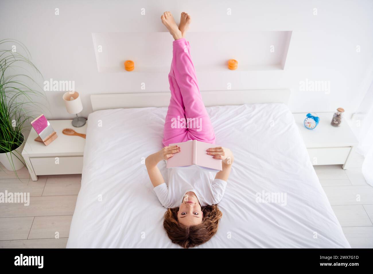 Full body photo of carefree cheerful girl lay upside down cozy bed hold ...