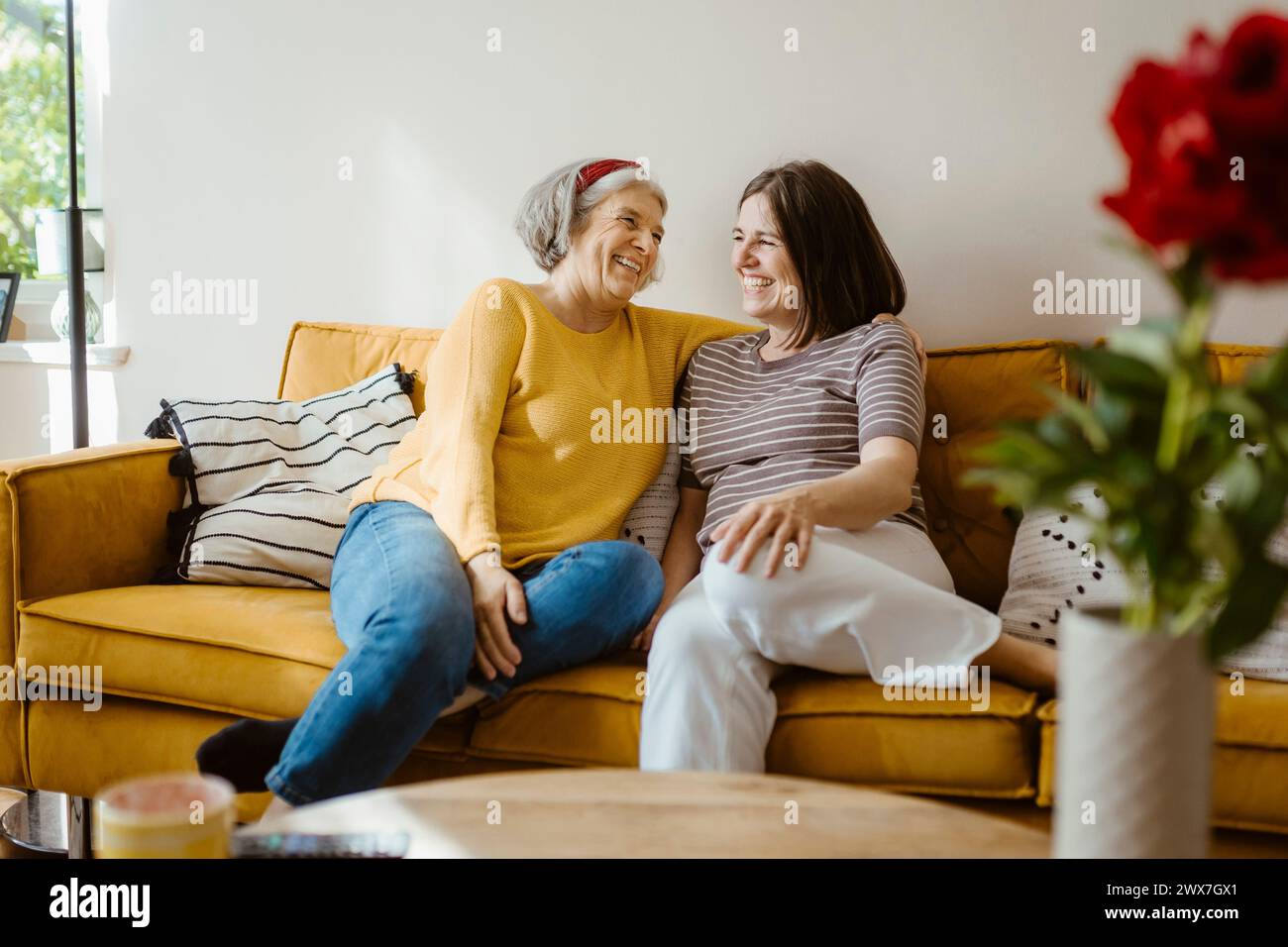Happy senior woman talking with daughter-in-law while sitting on sofa at home Stock Photo
