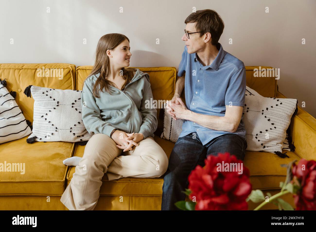 Mature man talking with teenage daughter while sitting on sofa at home Stock Photo