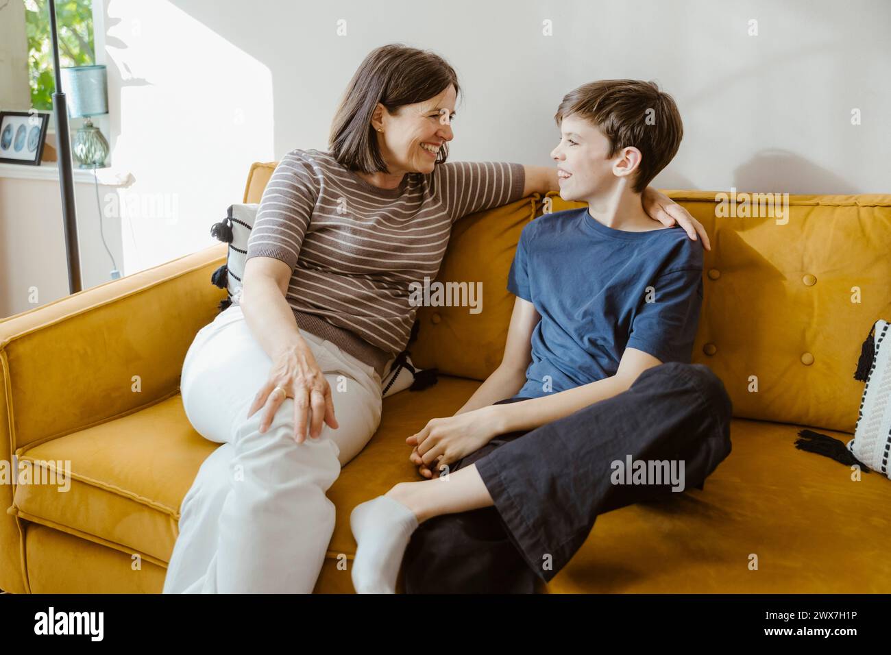 Smiling woman talking with son while sitting on sofa at home Stock Photo