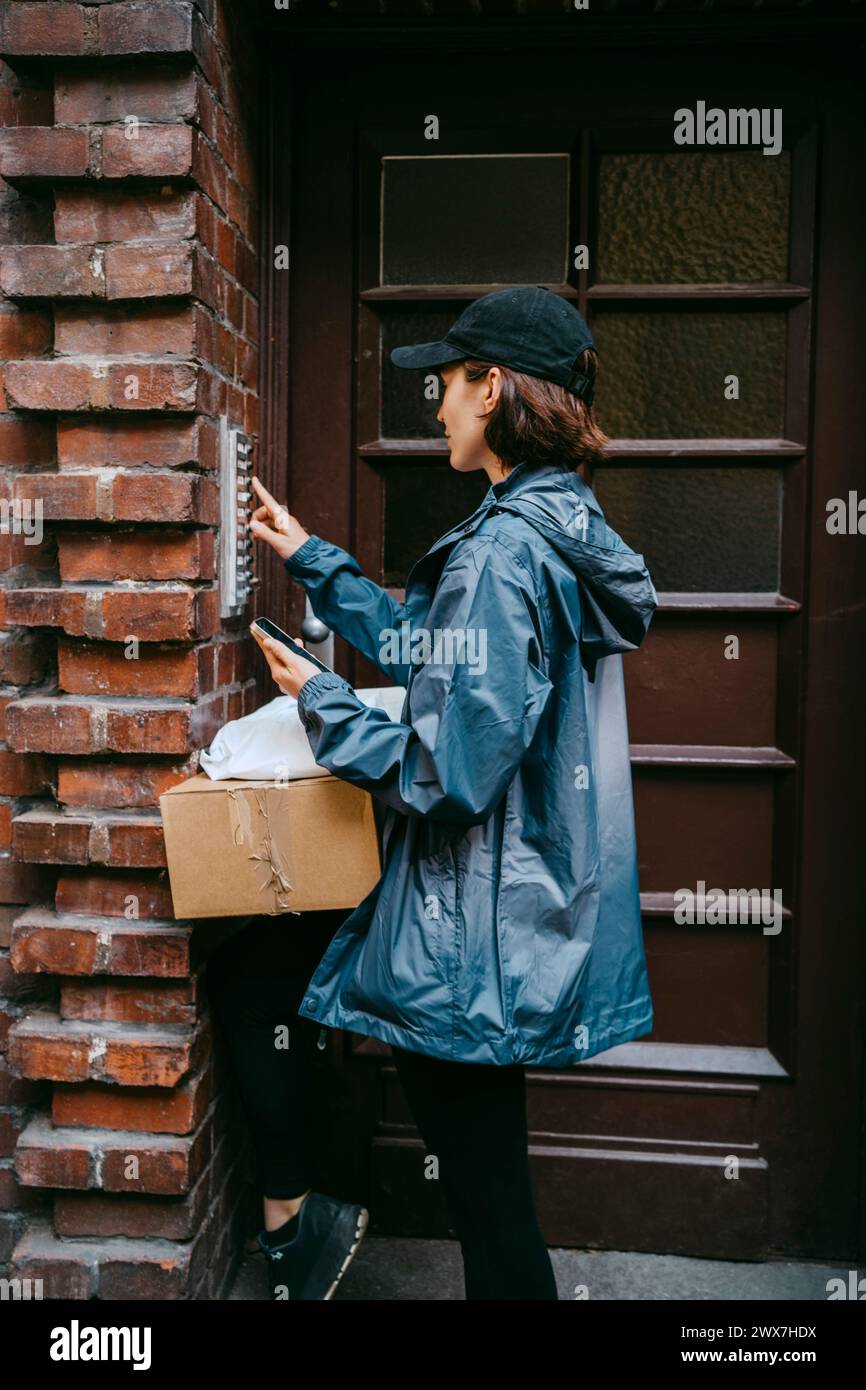 Side view of female courier delivery person ringing doorbell while arriving at doorstep Stock Photo