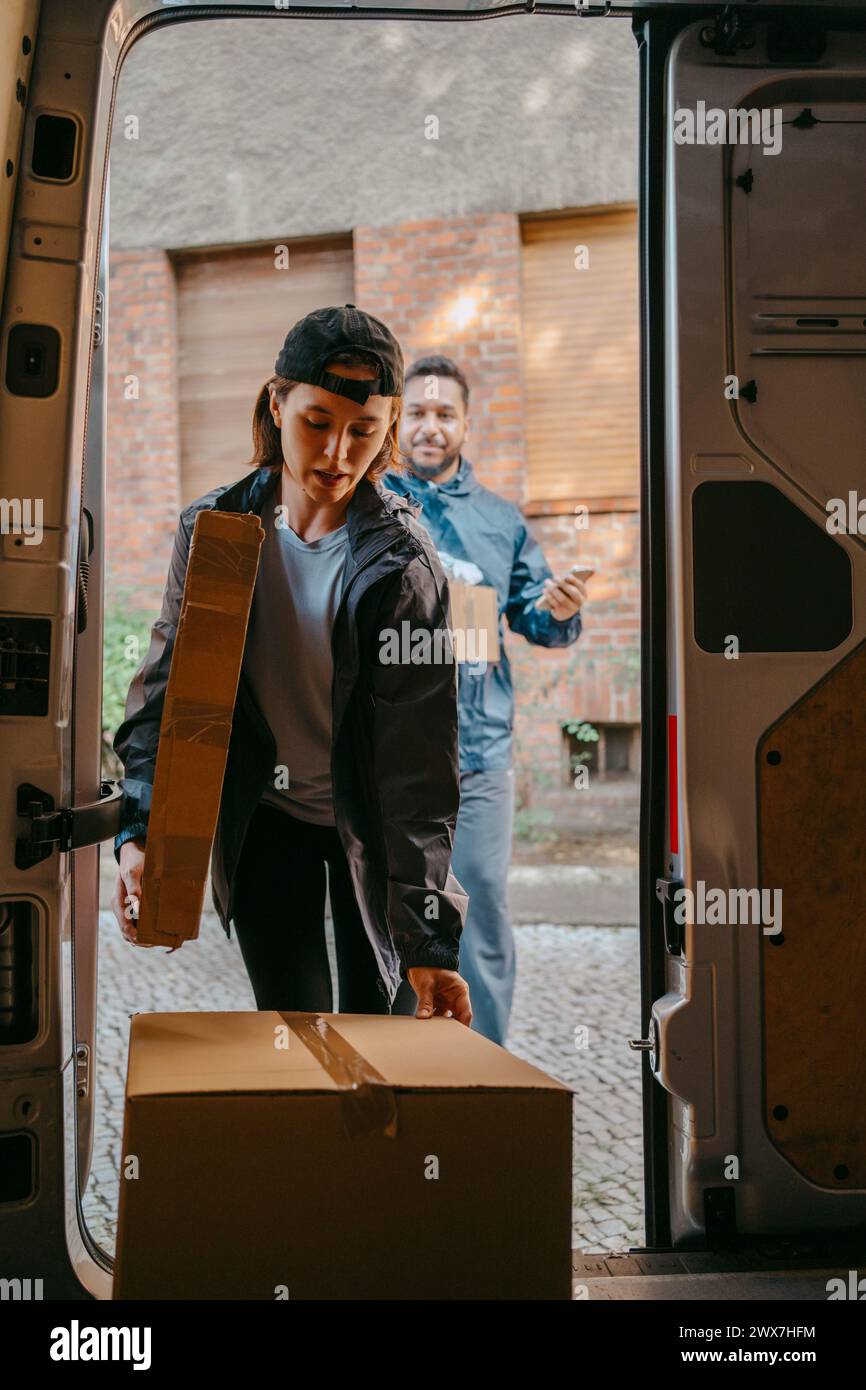 Male and female delivery coworkers unloading boxes from van trunk Stock Photo