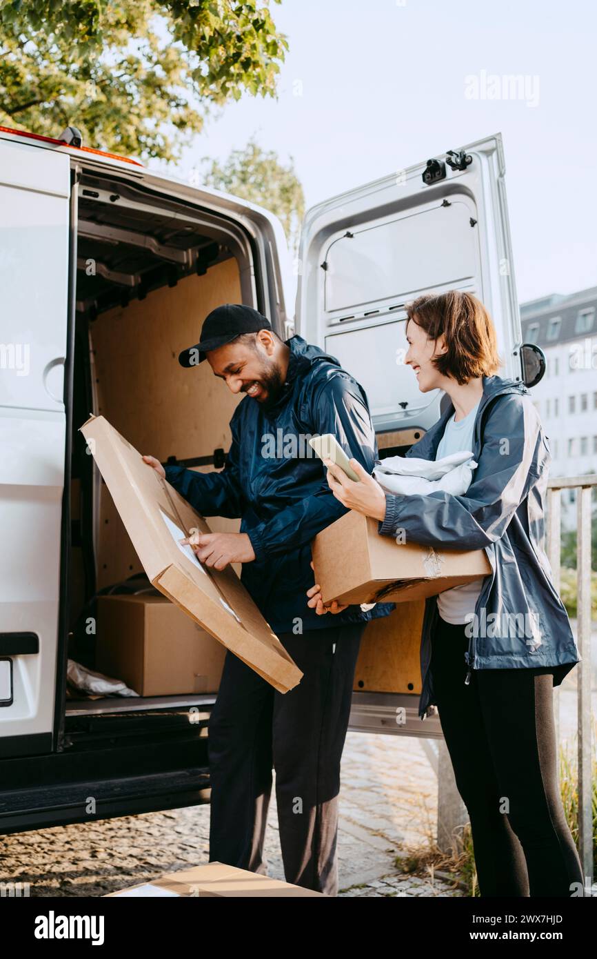 Male and female delivery coworkers unloading parcels from van trunk Stock Photo