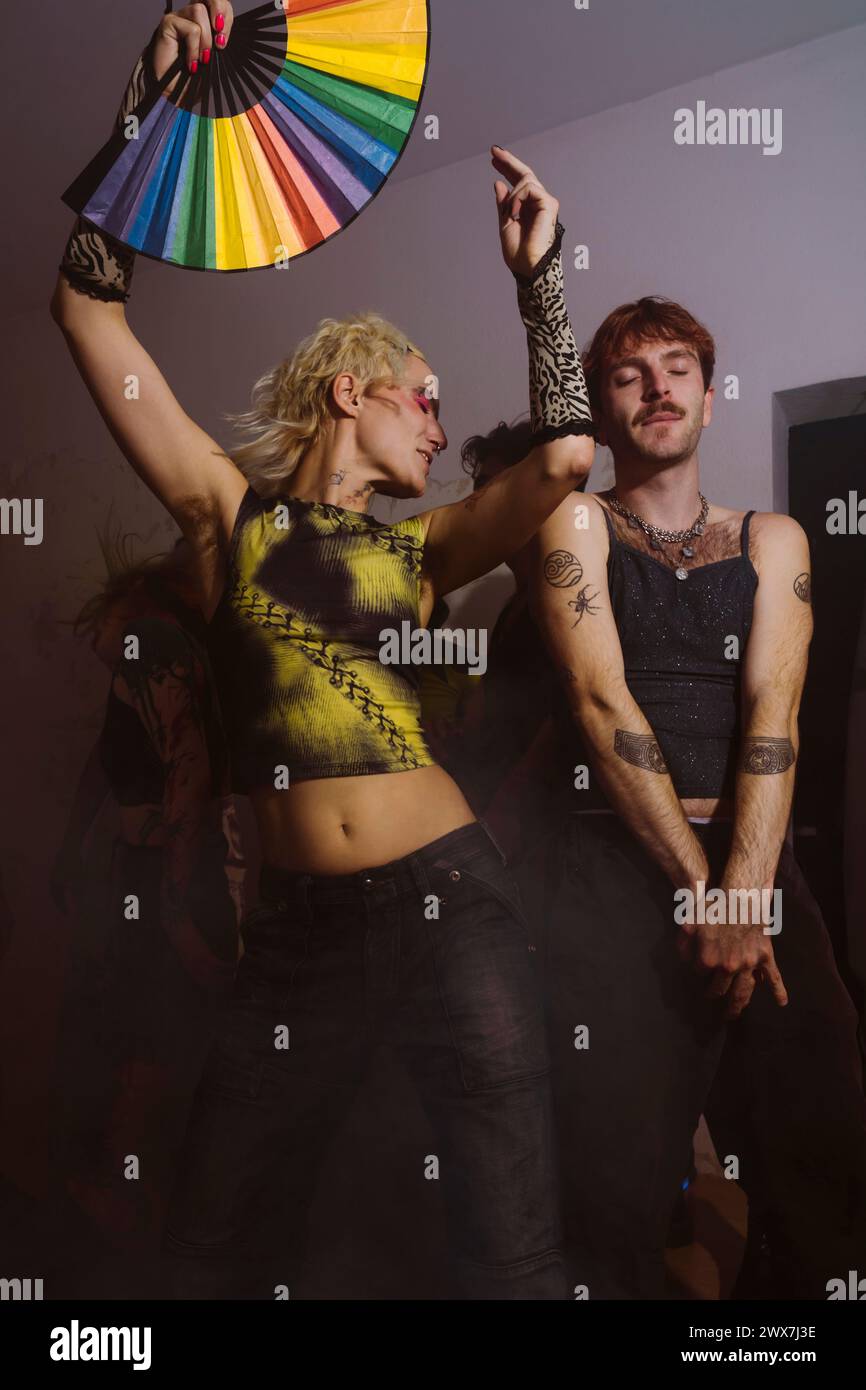 Carefree non-binary person holding hand fan and dancing next to gay ...