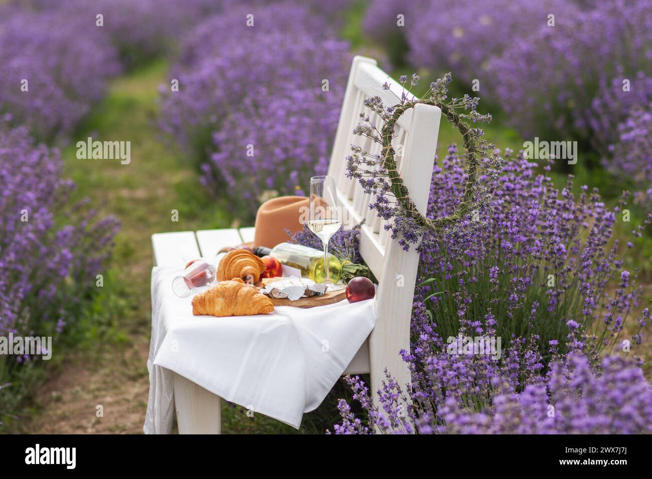 A summer picnic in a lavender field with croissants, peaches, salami, cheese and a bottle of wine and glasses. Violet flowers on the background. Stock Photo