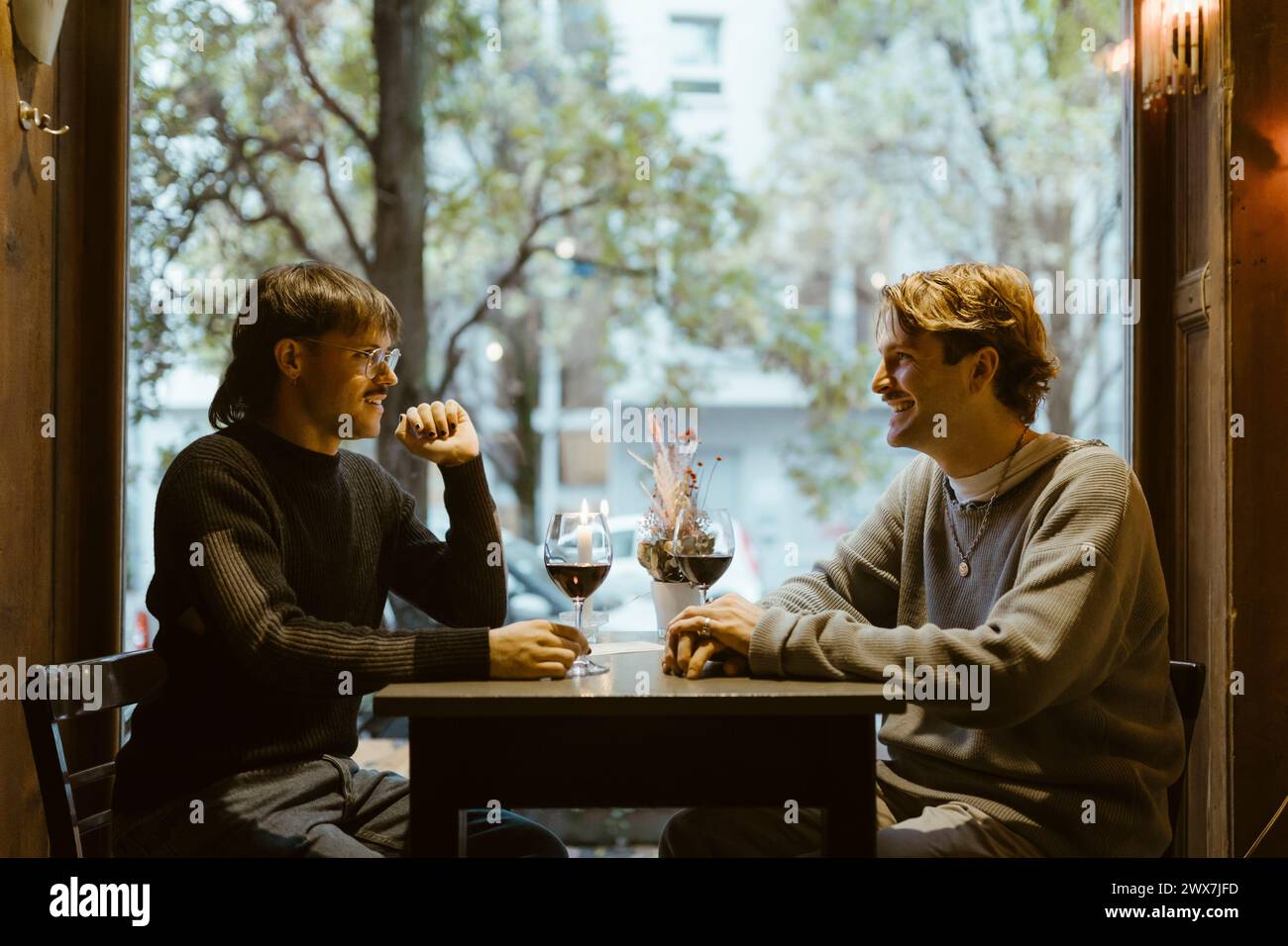 Happy gay couple talking while sitting with wineglasses on table during date at restaurant Stock Photo