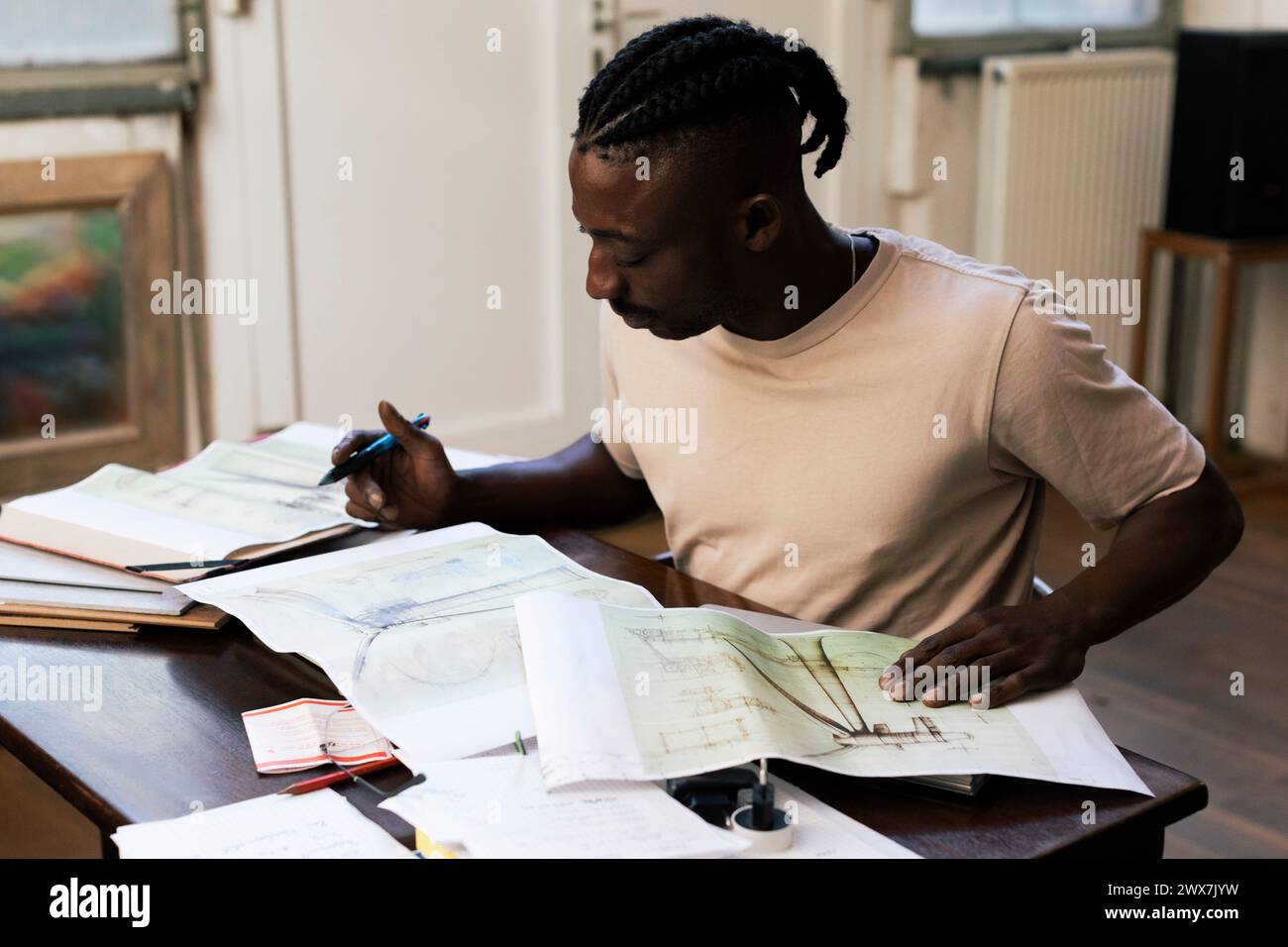 Focused male architect analyzing blueprints at table in workplace Stock Photo