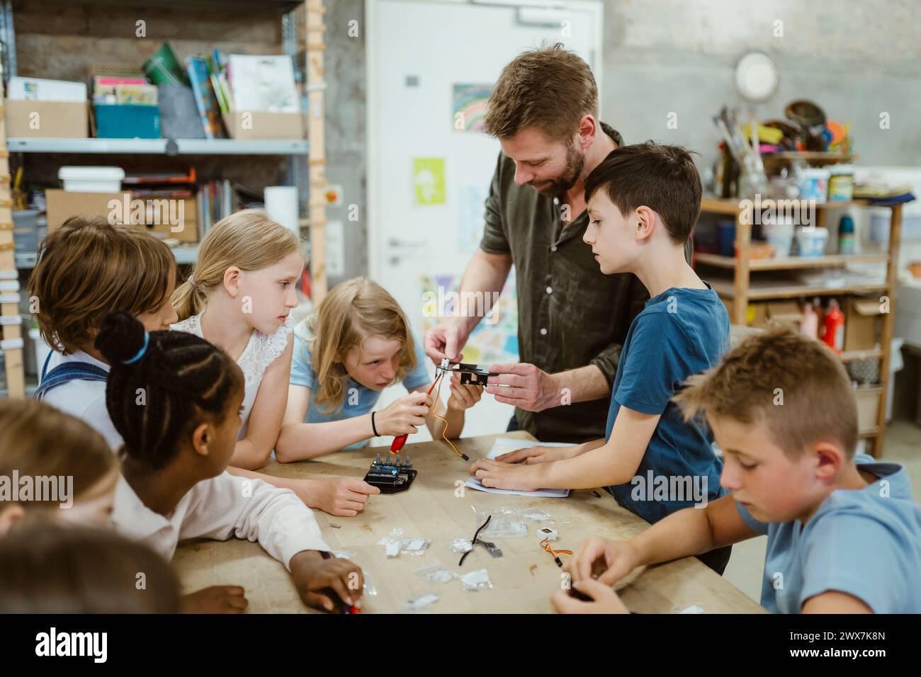 Male teacher helping students while working on robotics project at workshop in school Stock Photo