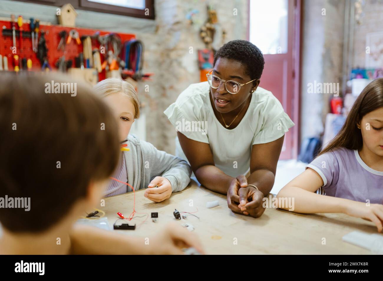 Female teacher leaning on table while teaching students during technology class Stock Photo
