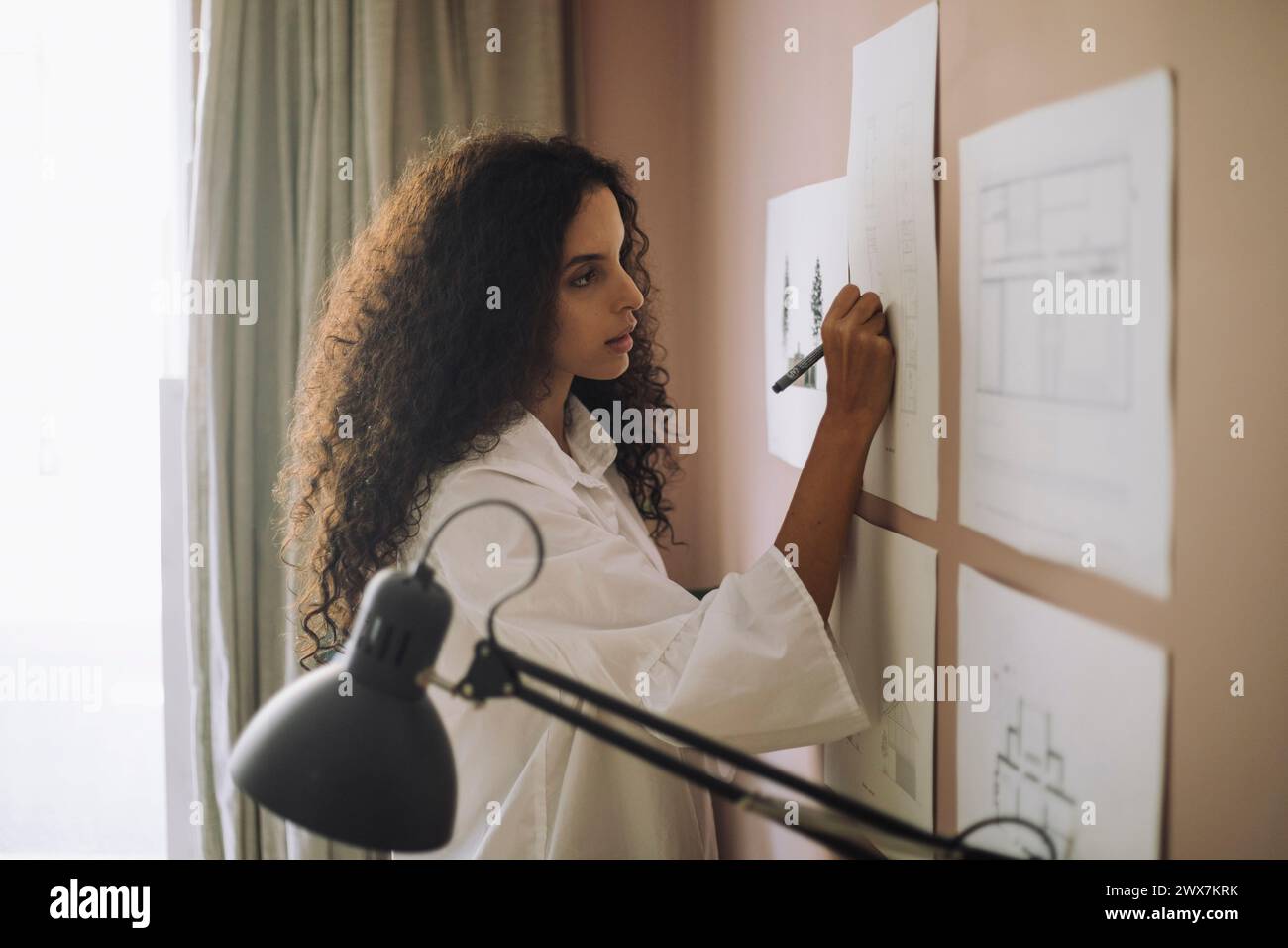 Focused female architect preparing blueprints on paper while working at office Stock Photo