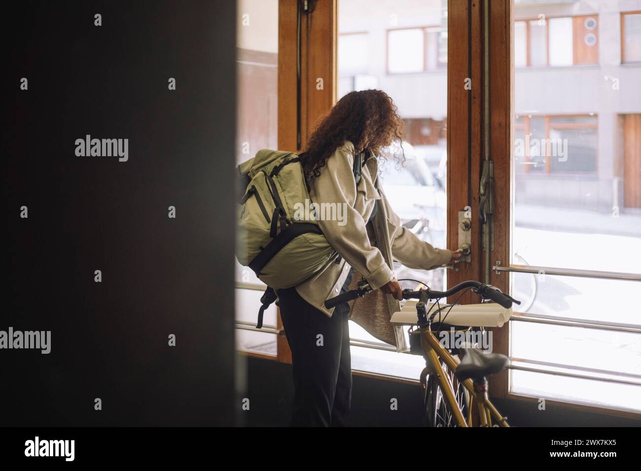 Side view of female freelancer opening door while leaving from building with bicycle Stock Photo