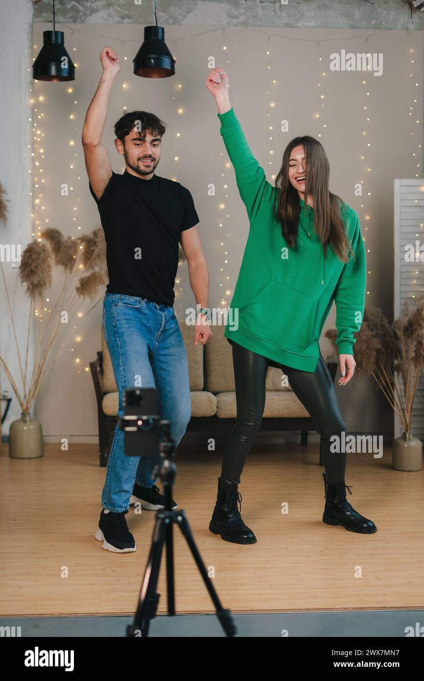 Happy man and woman recording dance moves on cellphone web camera, streaming live video in social network at home. Sharing professional skills online. Stock Photo