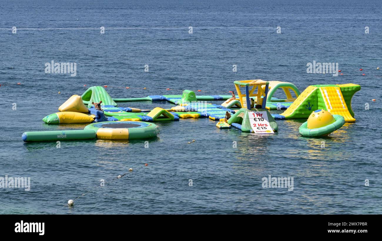 Malta - 4 August 2023: People playing on inflatable play equipment in the sea for tourists. Stock Photo