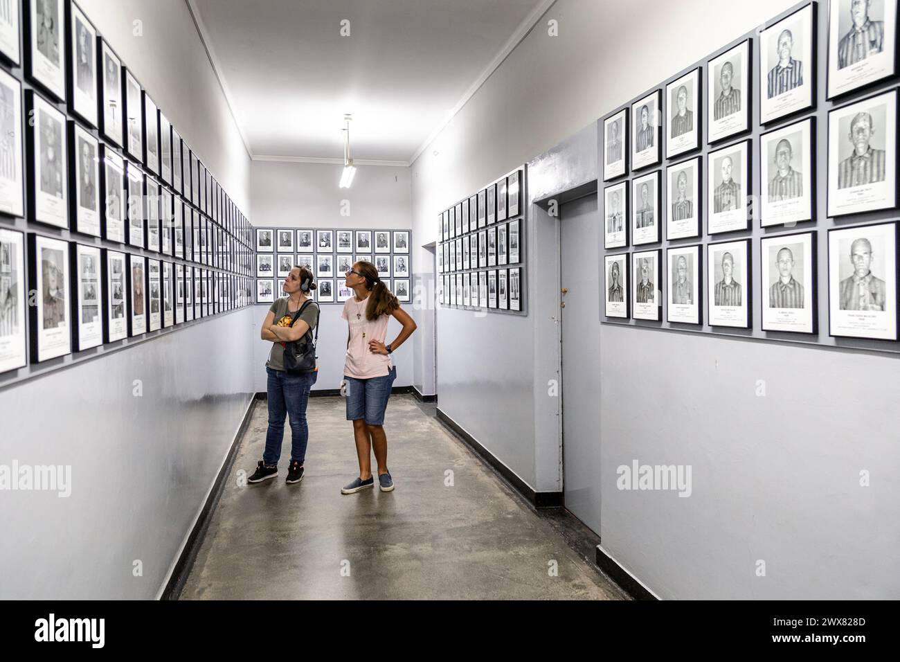 Two women looking at exhibition of photos of prisoners at the Auschwitz I concentration camp museum, Poland Stock Photo