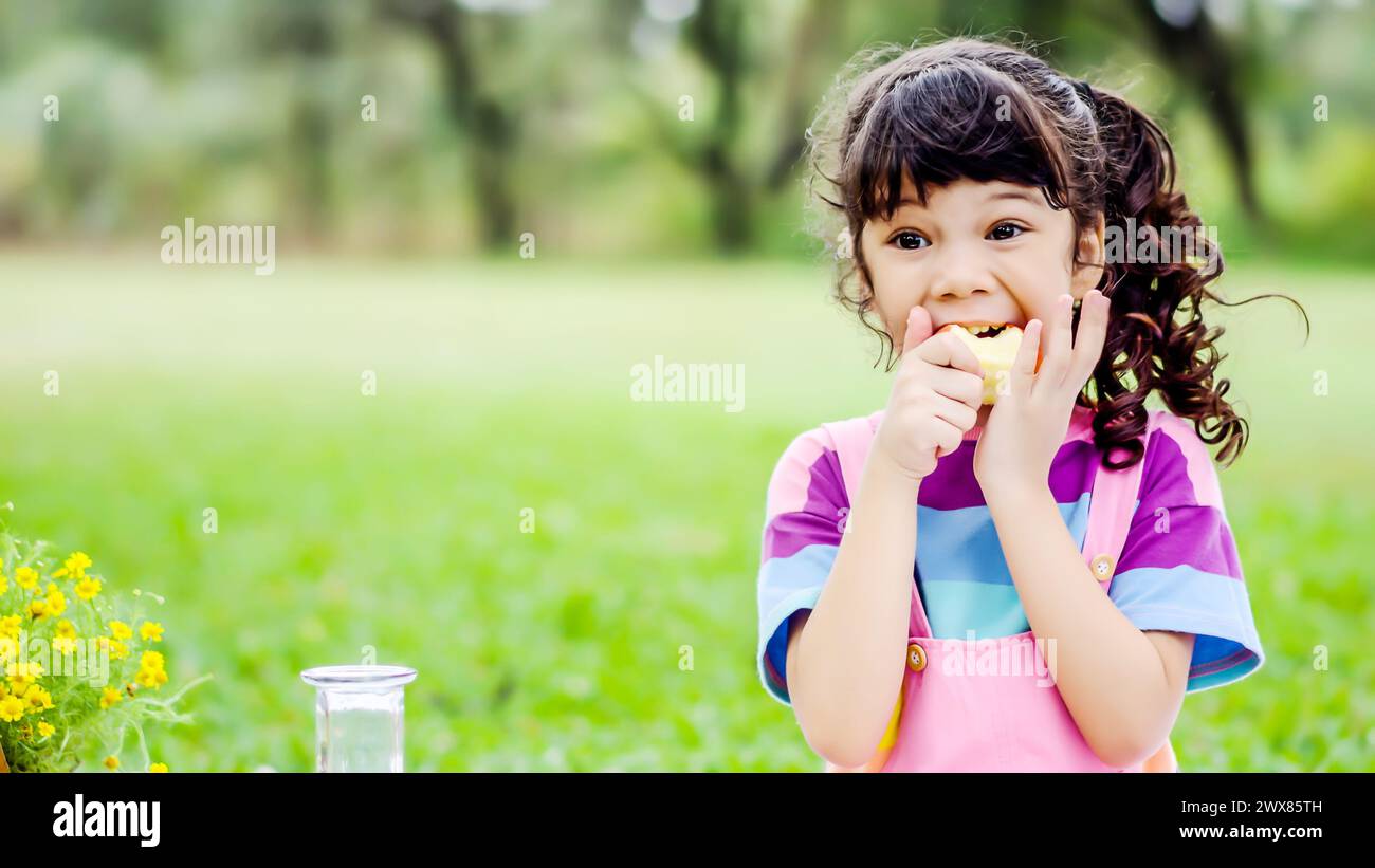 Young female enjoying an apple by a metal bin in the park Stock Photo