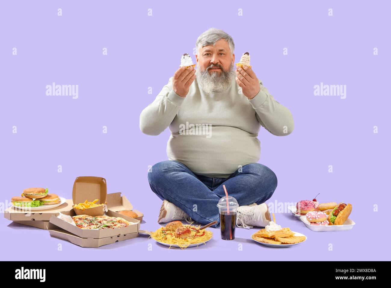 Overweight mature man with unhealthy food sitting on lilac background. Overeating concept Stock Photo
