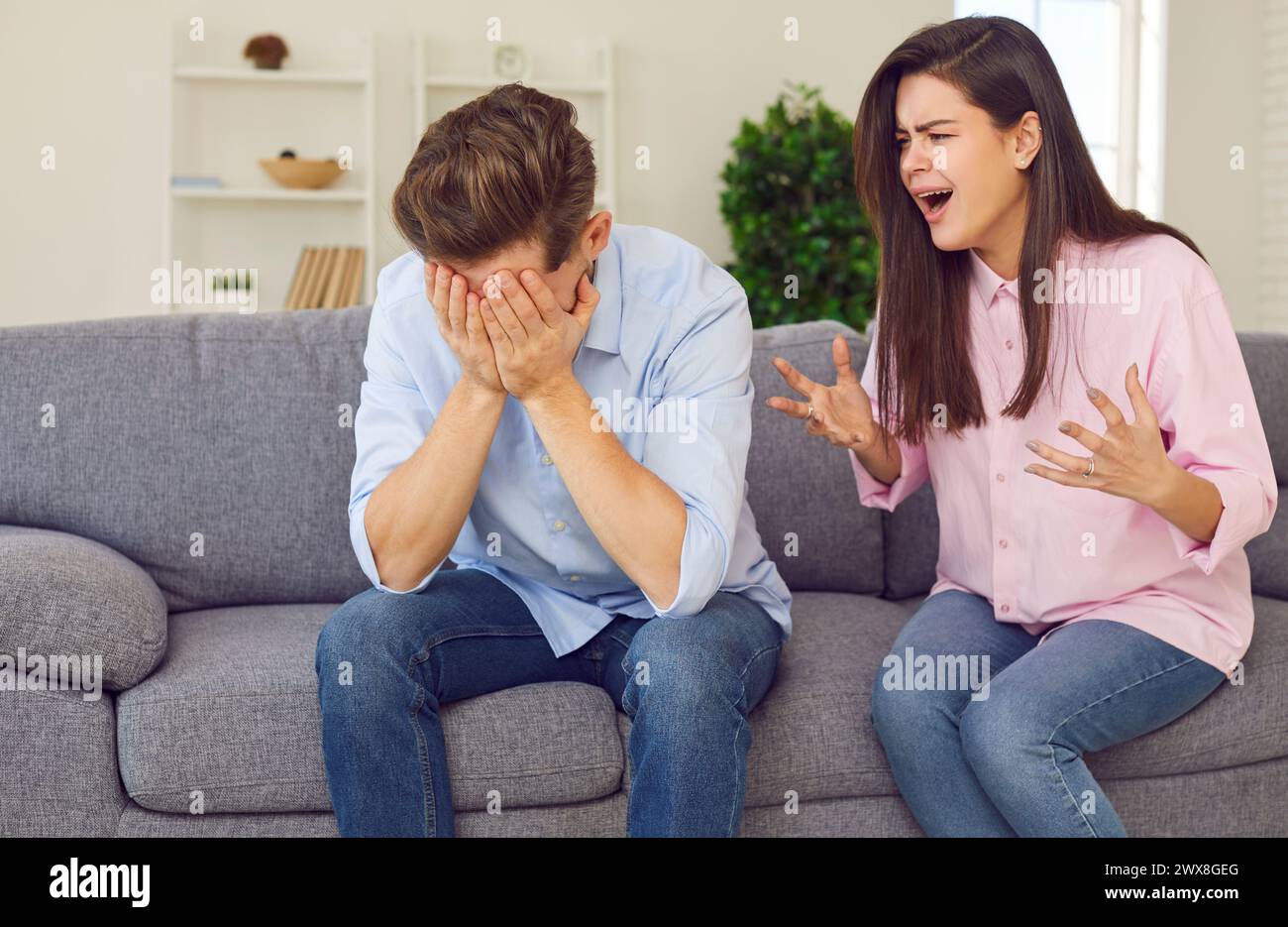 Woman shouts at man who covers his face with his hands, showing gesture of suffering or shame. Stock Photo