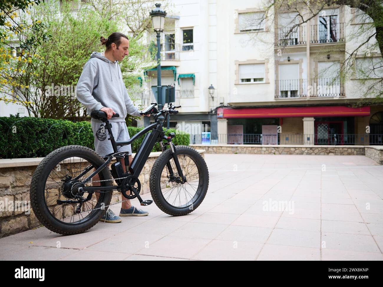 Young Caucasian man in sports wear, renting and riding e-bikes in the city. Electric bike bicycle as comfortable ecological mode of urban transport. B Stock Photo