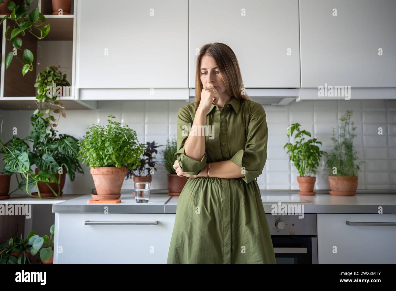 Disappointed thoughtful worried woman sadly looking thinking of problem standing at home on kitchen. Stock Photo